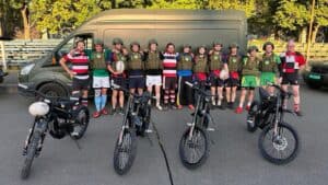 Rugby players posing in kits and body armour behind four donated electric motorcycles delivered in a Protect Ukraine convoy.