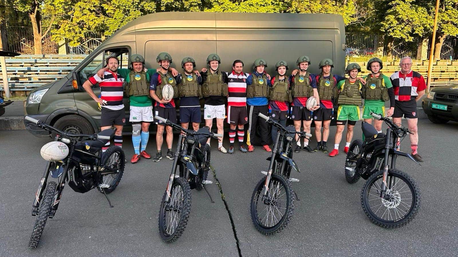 Rugby players posing in kits and body armour behind four donated electric motorcycles delivered in a Protect Ukraine convoy.