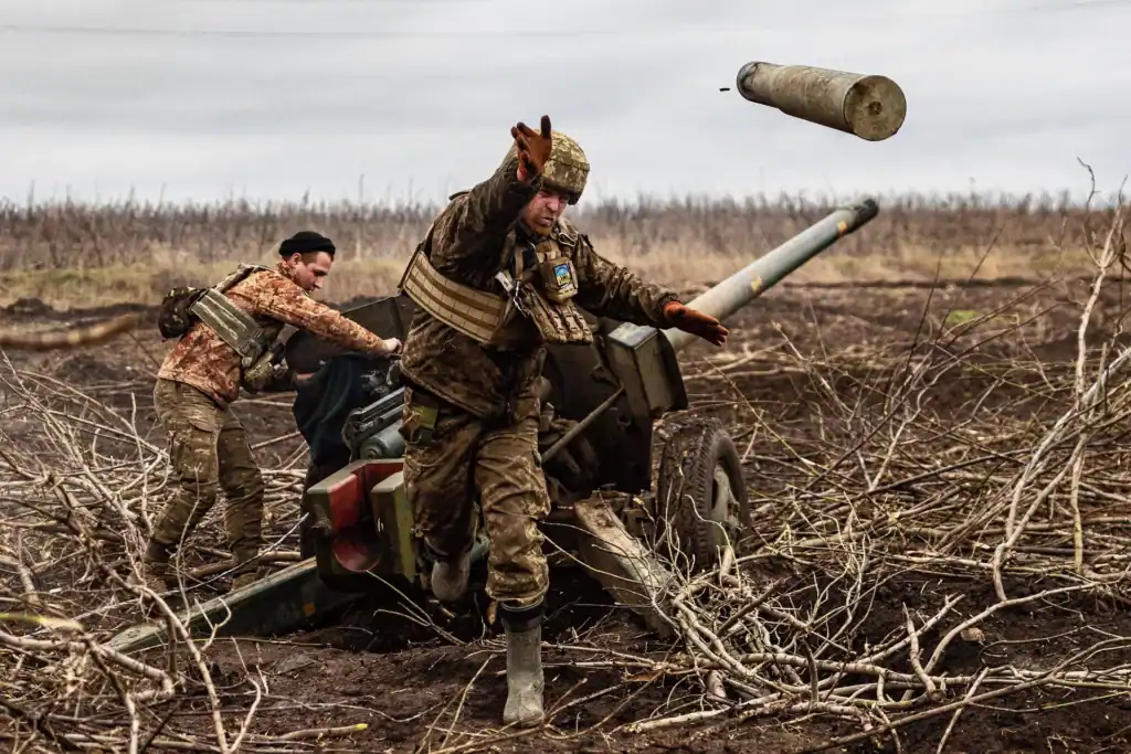 Soldiers operating an artillery gun during the war in Ukraine, with an empty shell casing flying mid-air.
