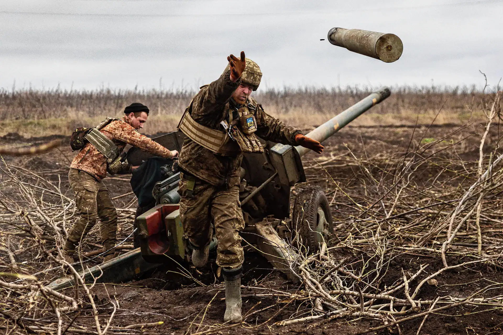 Soldiers operating an artillery gun during the war in Ukraine, with an empty shell casing flying mid-air.